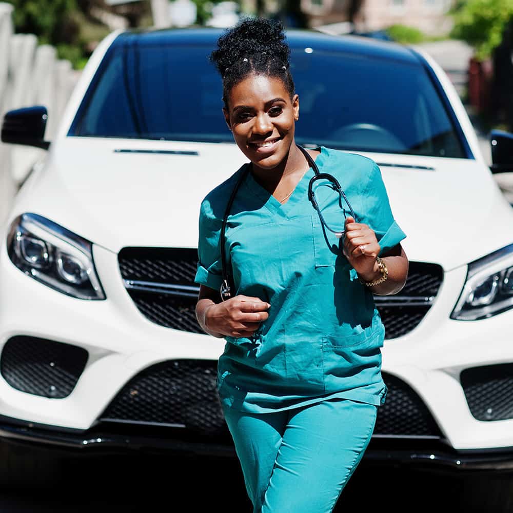 Young black nurse standing near new car.