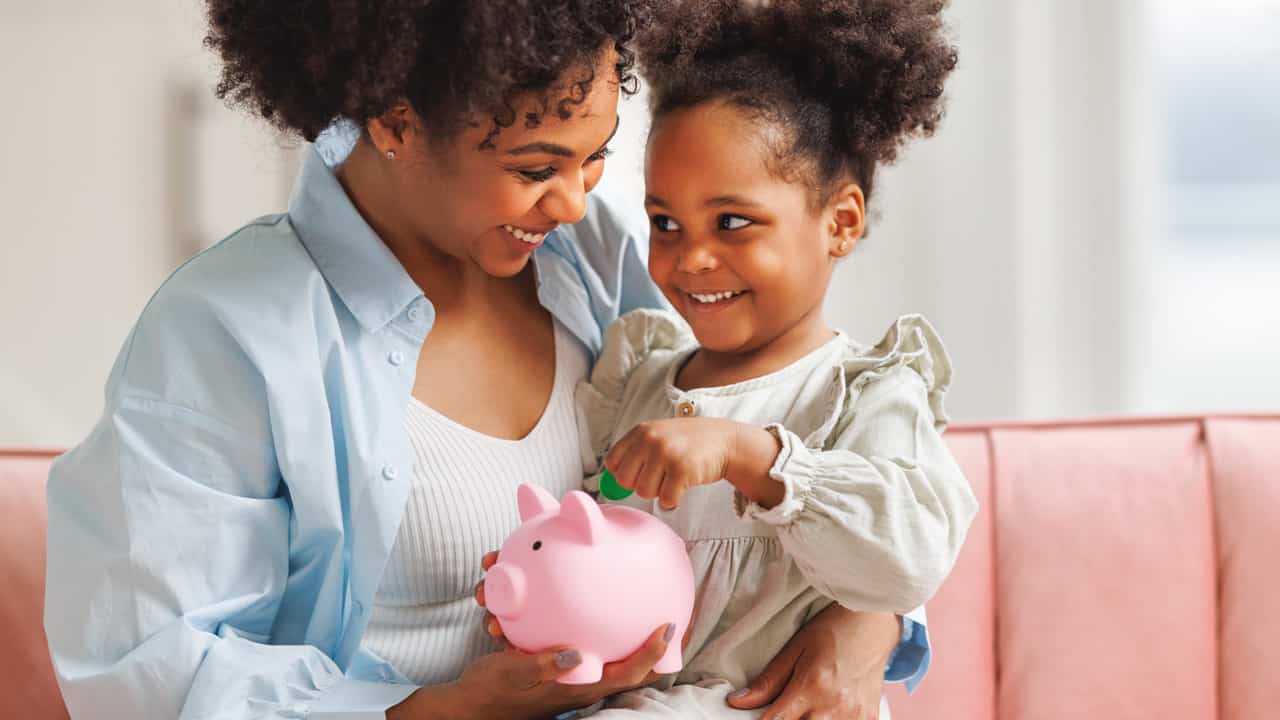 Young mon with her young daugher looking at a piggy bank.