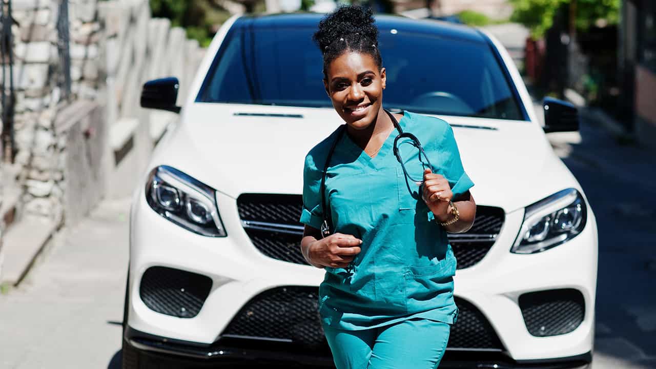 Young female nurse standing in front of car in her scrubs.