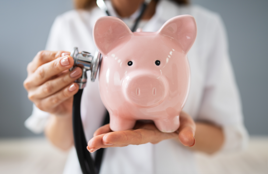 Stethoscope on Piggy Bank in Doctors Hand